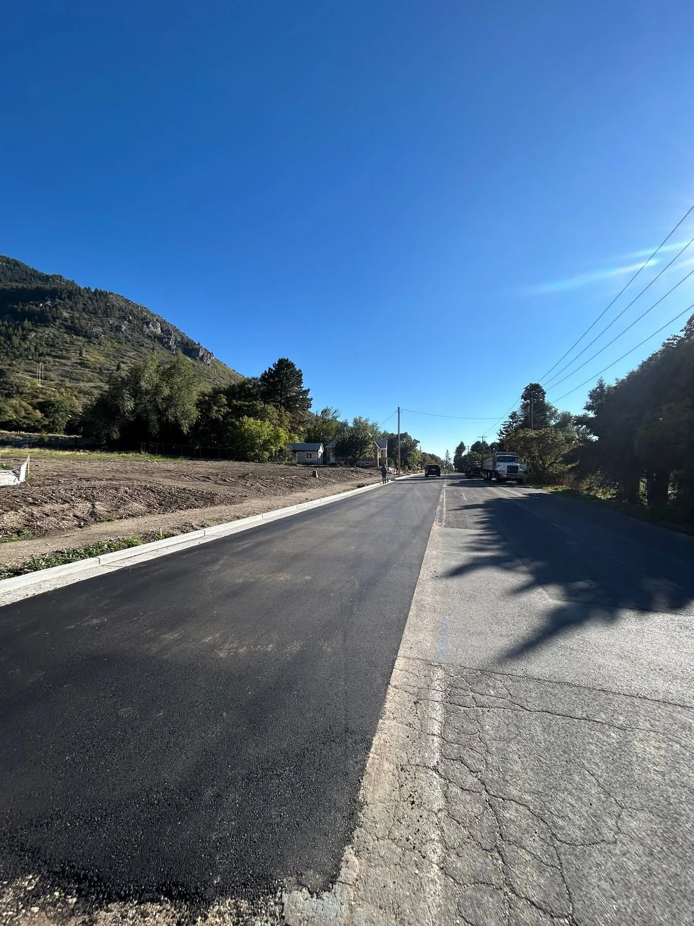 A freshly paved asphalt road beside a graded lot in a mountain canyon