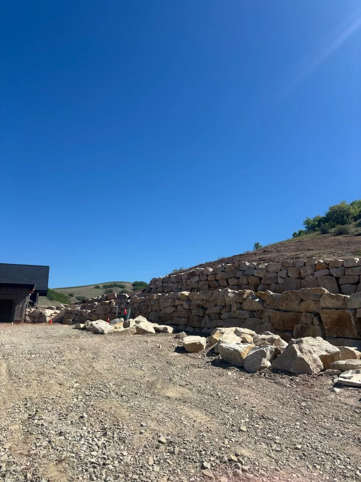 A completed boulder retaining wall lining a graded building pad under a clear blue sky