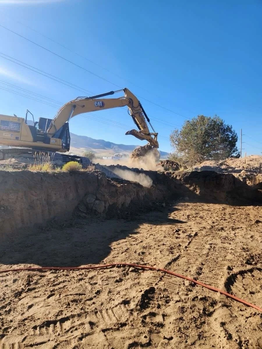 A CAT excavator digging a large pit against a clear blue sky